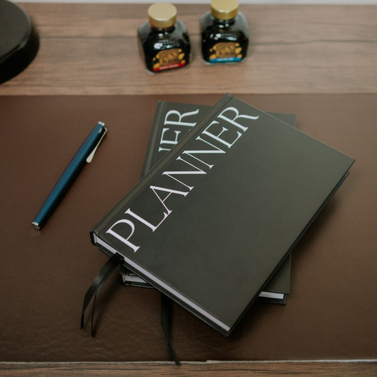 Two Arden Classic Black 100 day productivity planners on a desk with a pen.