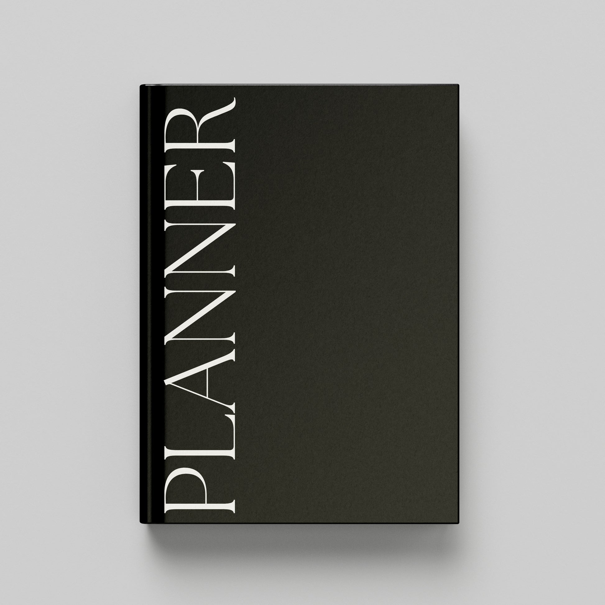A black hardcover planner with the word 'PLANNER' printed vertically in white serif lettering on the front cover, shown against a light grey background.