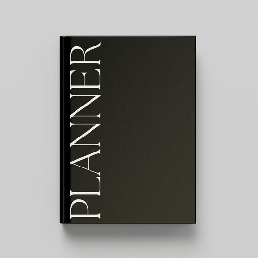 A black hardcover planner with the word 'PLANNER' printed vertically in white serif lettering on the front cover, shown against a light grey background.