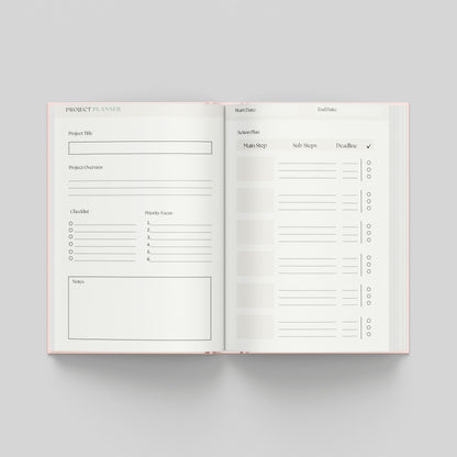 An open planner showing two interior pages for a project planner, photographed from above on a light grey background. The pages are white with thin black lines and text, and the planner edges are pale pink.