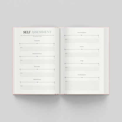 An open hardcover journal or planner on a light grey background, showing two white pages with printed self-assessment review sections to see where you are now to look back on in the future.